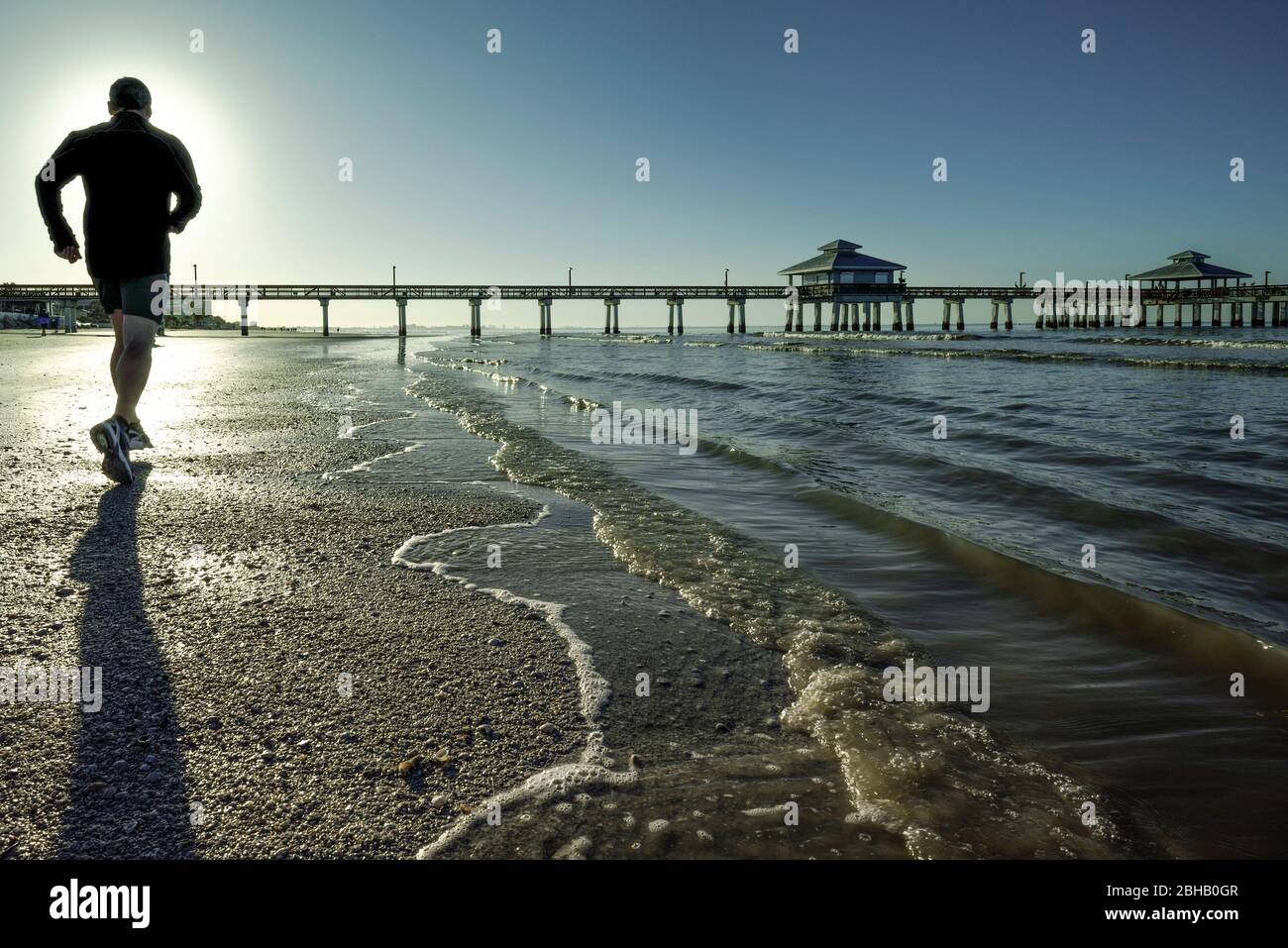 Jogger de derrière à la matinée courir dans la zone de surf à la plage de fort Meyers avec jetée en arrière-plan Banque D'Images