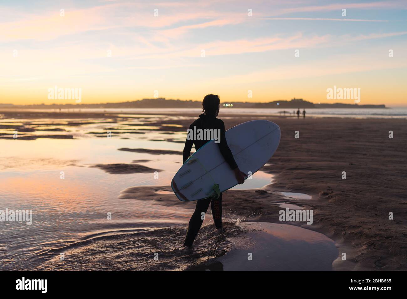 Les jeunes surfeurs mâles marchent sur le sable de plage au coucher du soleil avec planche sous son bras Banque D'Images