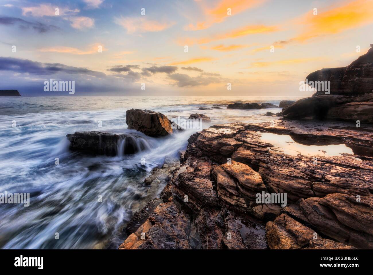 Rochers de grès avec galet d'eau salée de marée au lever du soleil face à l'est sur les plages du nord de Sydney et la côte du Pacifique. Banque D'Images