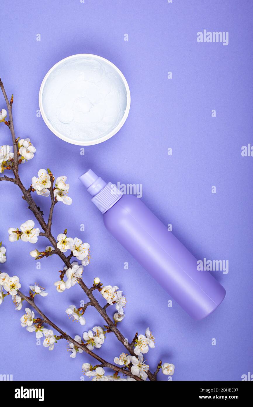bouteilles avec cosmétiques de soins du corps avec fleurs blanches sur fond violet vue de dessus. Banque D'Images