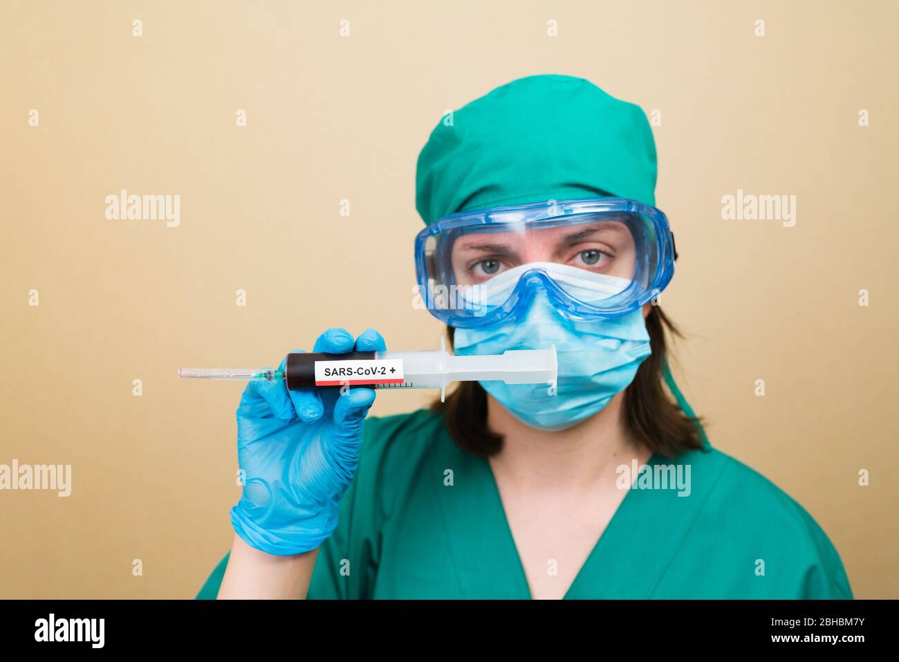 Le médecin féminin en costume vert et les gants bleus contiennent un tube à essai avec du sang positif COVID-19 sur le fond jaune. Concept médical. Mise au point sélective. Banque D'Images