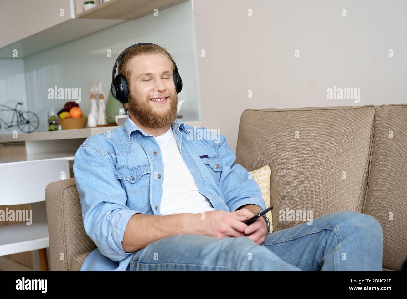 Un salon pour jeunes hommes décontracté sur un canapé porte un casque à écouter de la musique. Banque D'Images