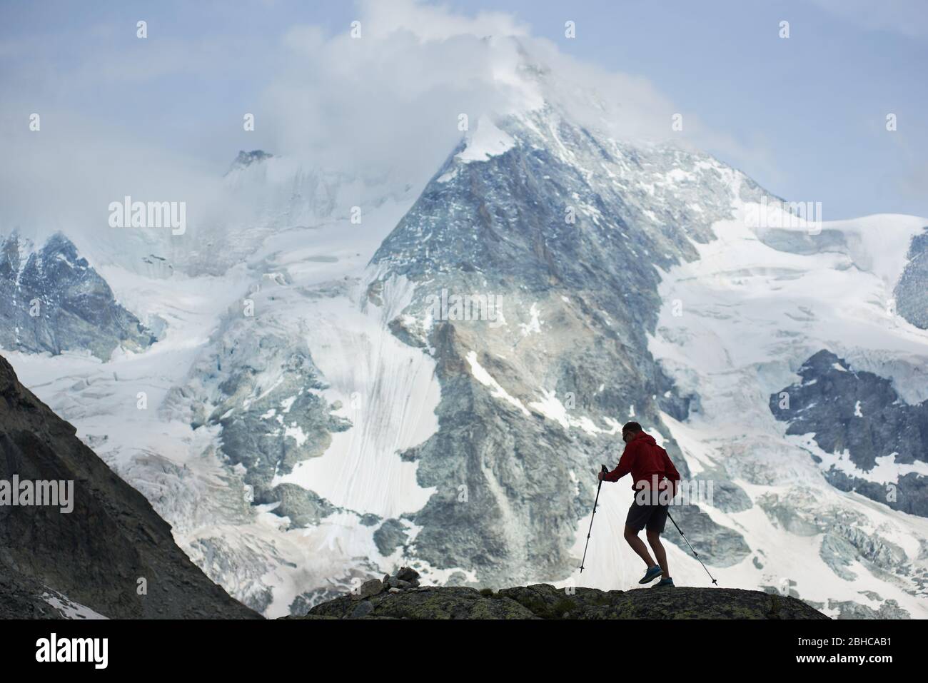Randonneurs mâles grimpant avec des bâtons de randonnée. Magnifique montagne rocheuse dans la neige dans les Alpes Pennine sur fond. Randonnée dans la montagne, homme atteignant le sommet. Nature sauvage avec une vue incroyable. Le tourisme sportif dans les Alpes. Banque D'Images