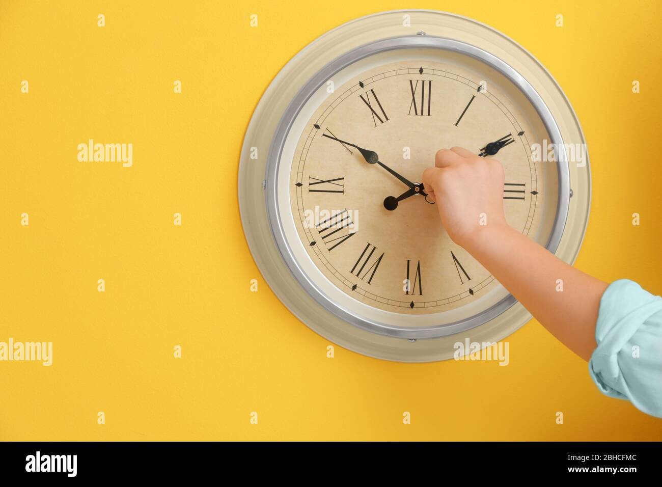 Petit garçon touchant des flèches de l'horloge sur le mur de couleur Banque D'Images