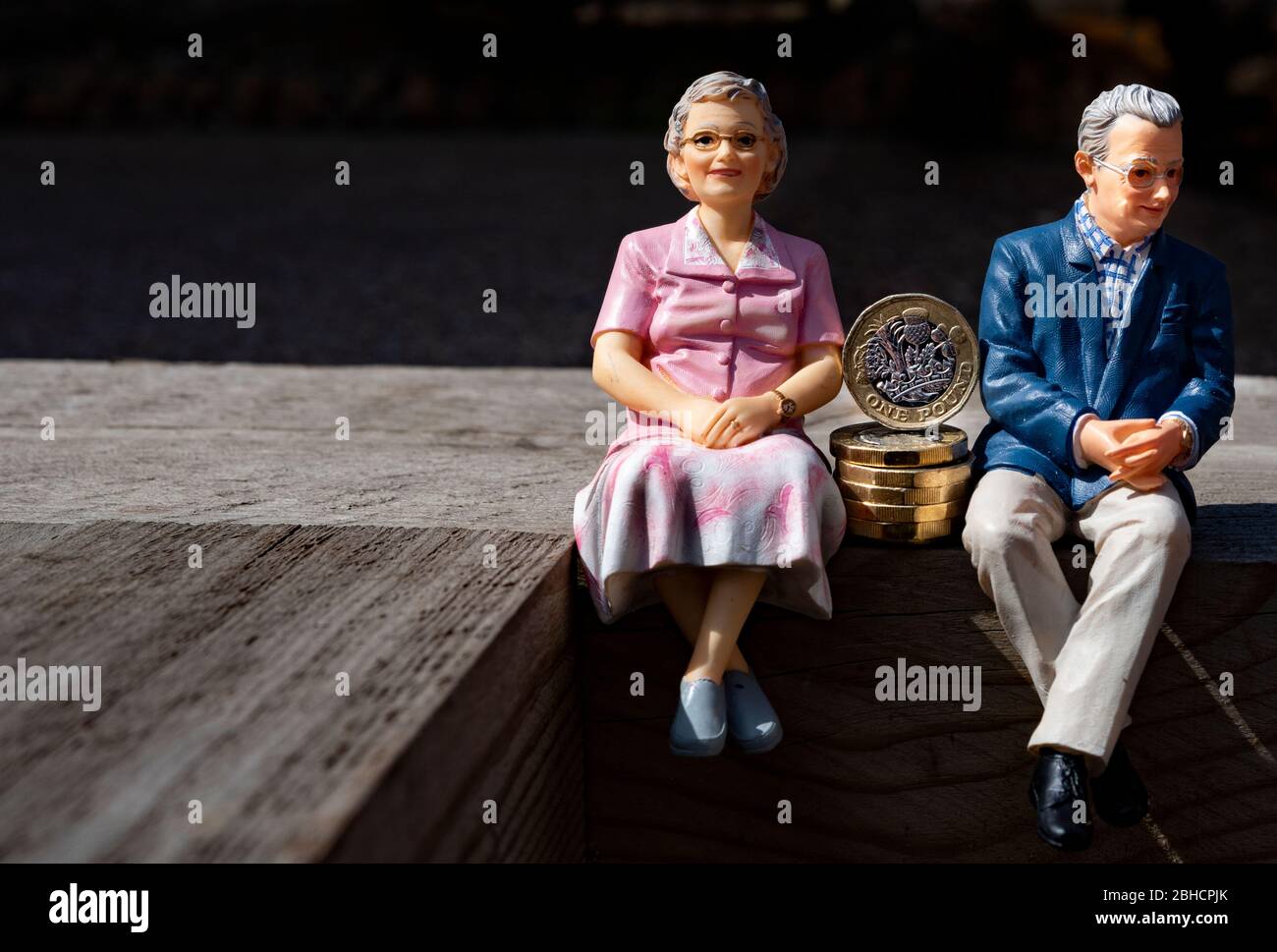 Couple de retraités, figurines miniatures, assis avec une livre de pièces, sur une surface en bois Banque D'Images