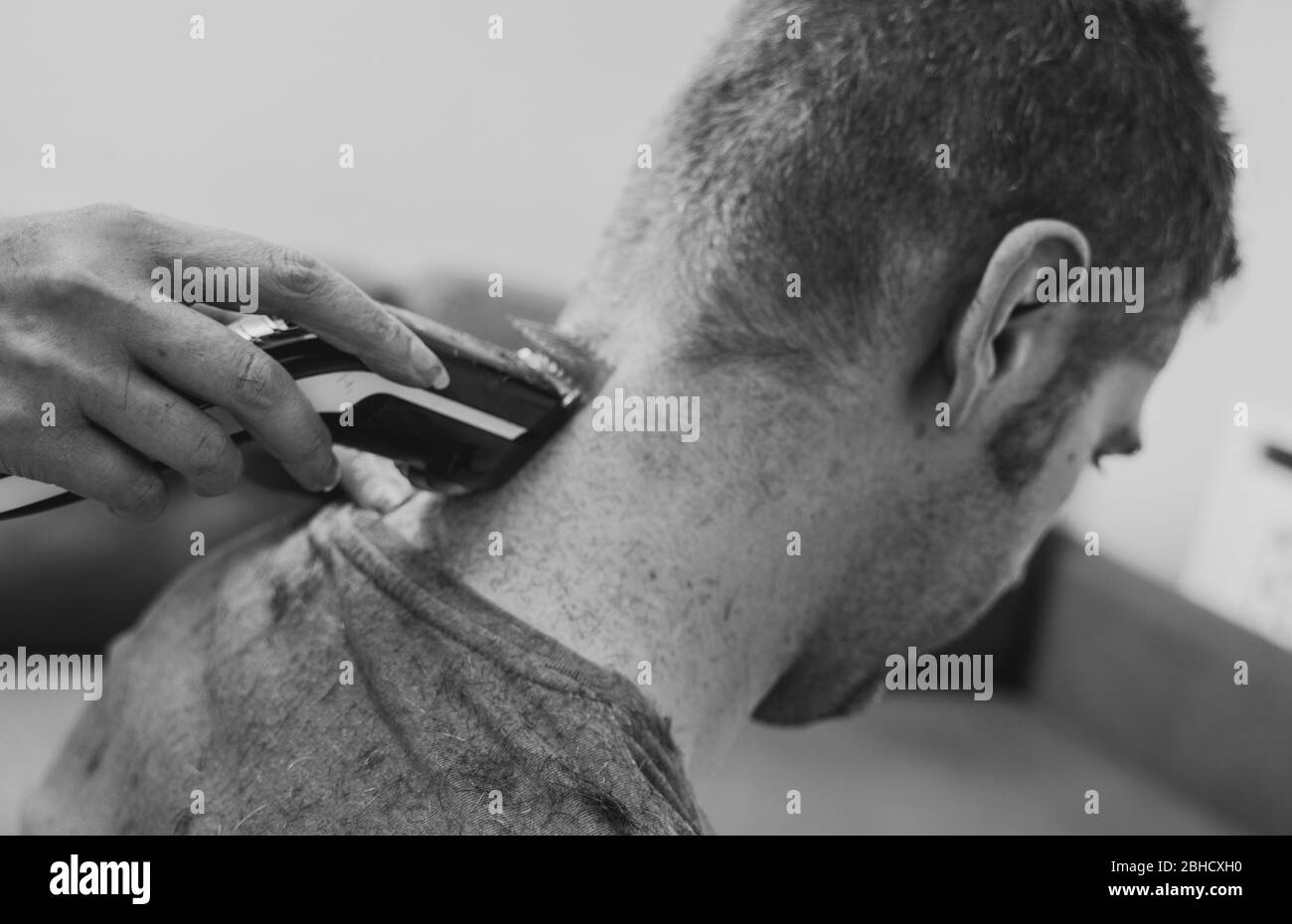 Femme fait coupe de cheveux avec la tondeuse à cheveux à l'homme à la maison. Photo en noir et blanc. Banque D'Images