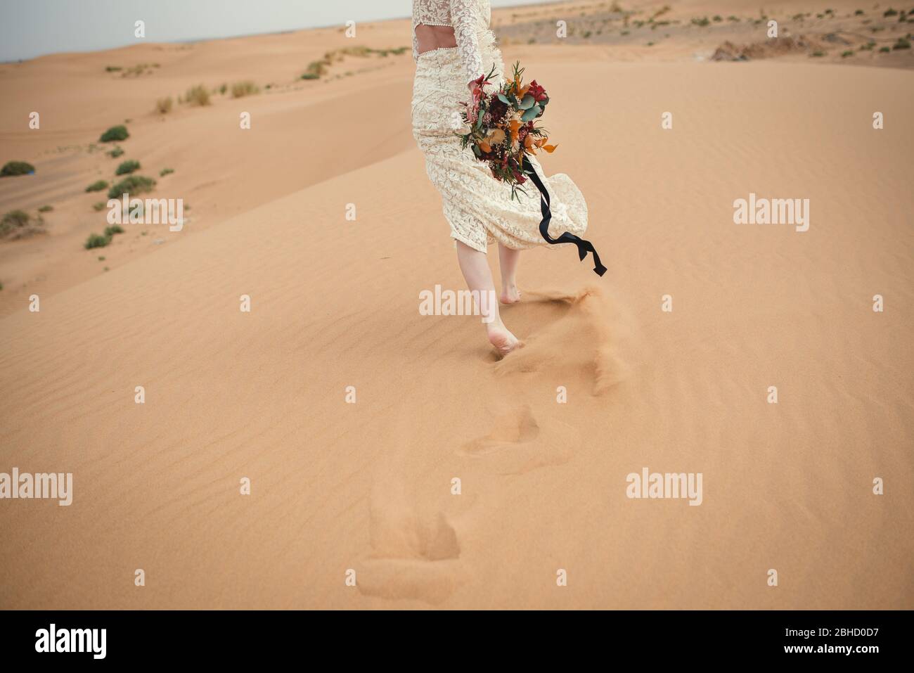 mariée marchant sur une dune de sable tenant des fleurs bouquet Banque D'Images