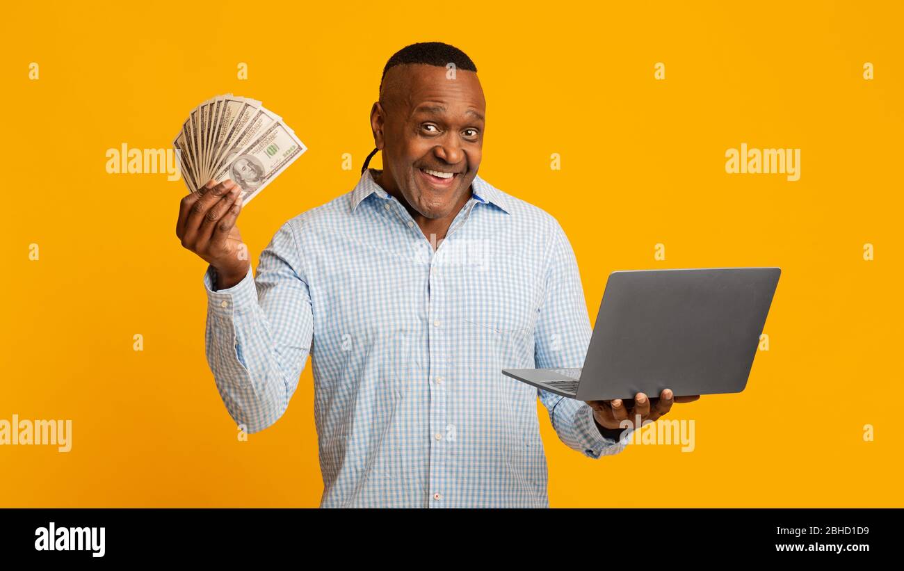 Homme africain excité et mûr, qui détient beaucoup d'argent et d'ordinateur portable Banque D'Images