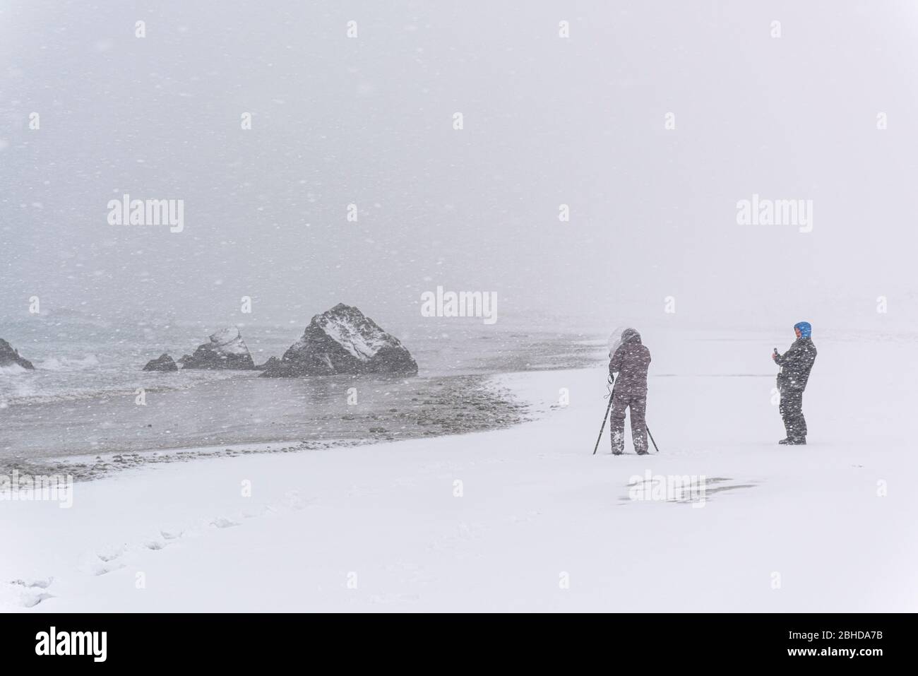 Personne imreconnaissable photographiant un rocher sur la plage lors d'une tempête de neige venteuse Banque D'Images