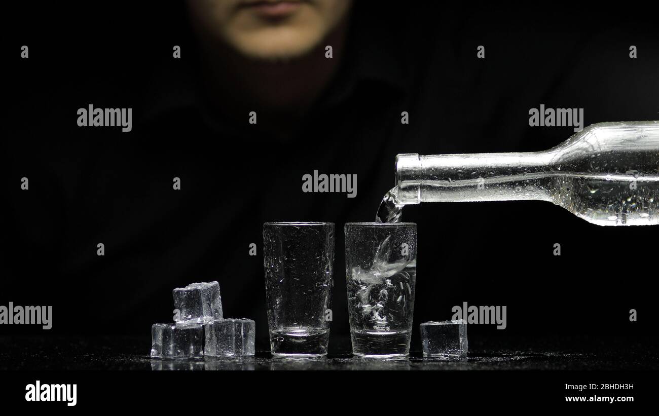 Barman verser de la vodka gelée d'une bouteille dans deux verres avec  glaçons sur fond noir. Barman pour boissons transparentes alcool rhum  tequila en verre Photo Stock - Alamy