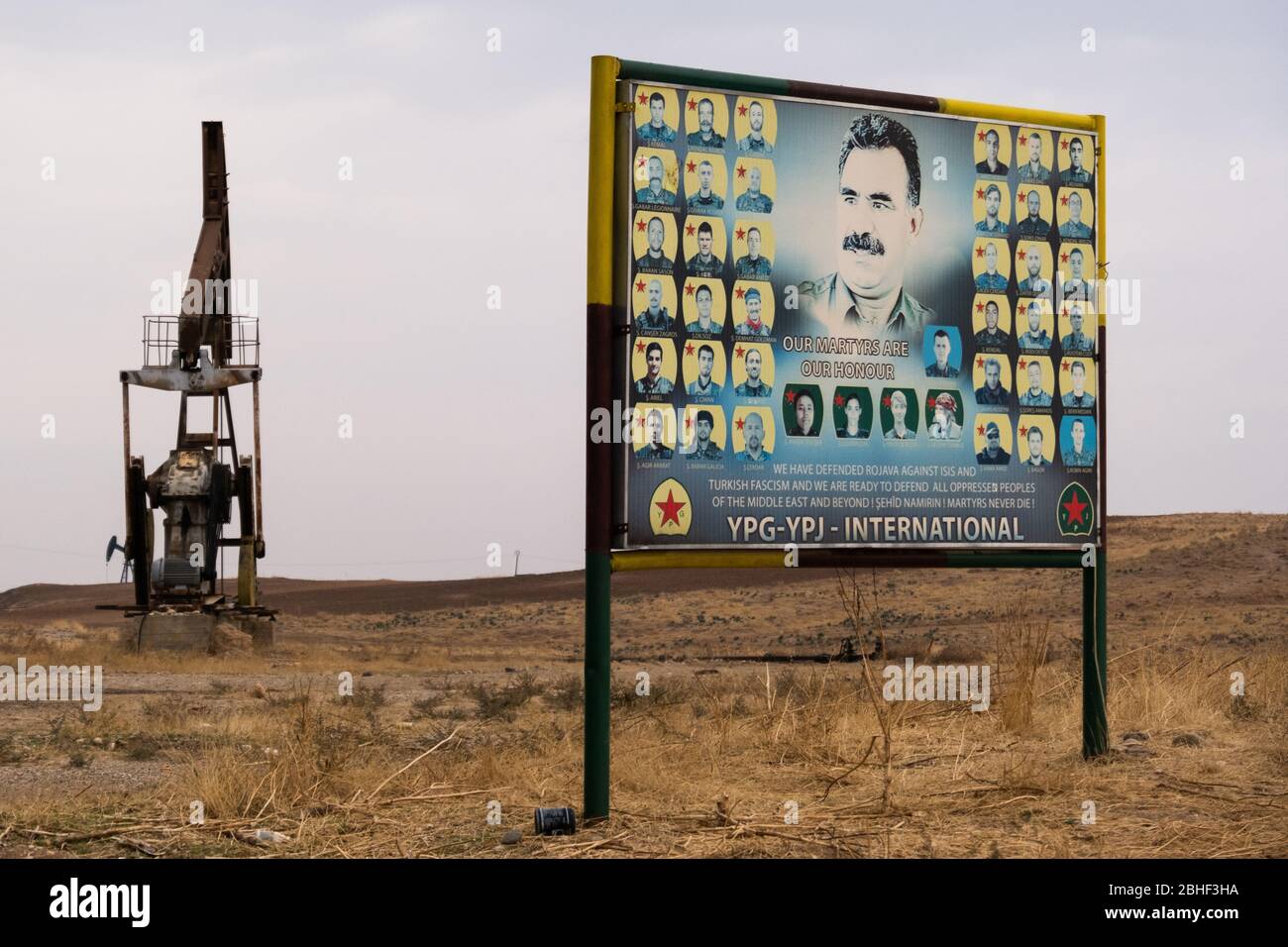Un panneau de commémoration des combattants internationaux qui ont combattu avec le YPG pendant le conflit syrien avec le fond du champ pétrolier de Rumeilan. Syrie du Nord-est. Banque D'Images