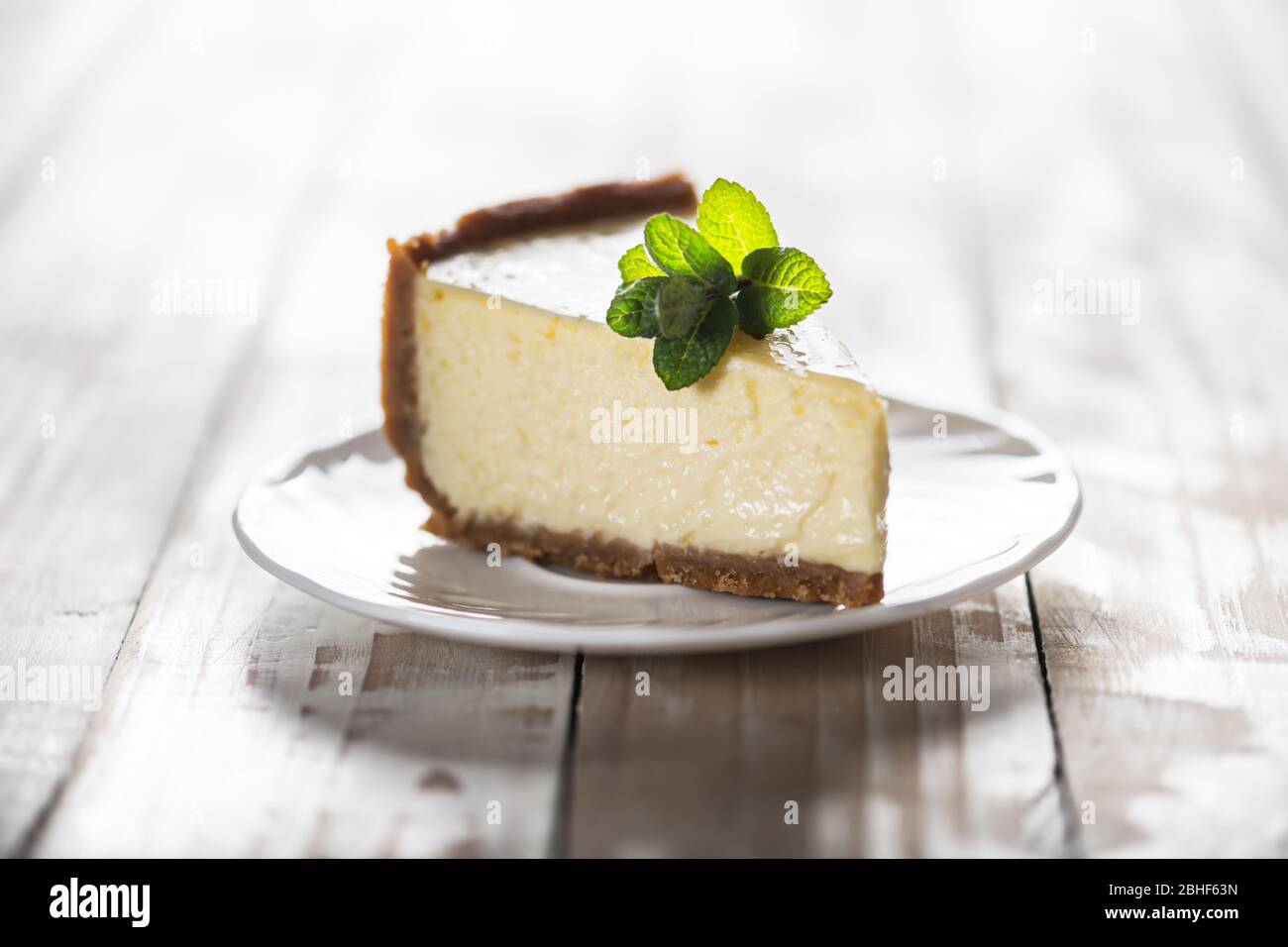 Tranche de cheesecake New York classique avec une branche de menthe sur une plaque sur une table en bois. Le concept de la boulangerie et des desserts aux gâteaux sucrés Banque D'Images