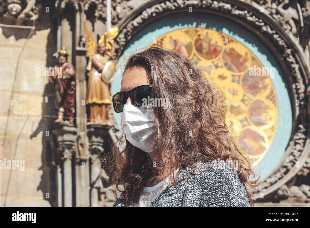 Jeune femme caucasienne avec lunettes de soleil et masque médical photographié devant l'horloge astronomique Orloj à Prague, en République tchèque. Voyager, tourisme pendant coronavirus. Concept COVID-19. Banque D'Images