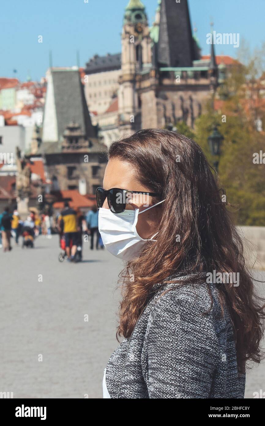 Jeune femme avec lunettes de soleil et masque médical photographié sur le pont Charles à Prague, République tchèque. Vieille ville floue à l'arrière-plan. Voyager, tourisme pendant coronavirus. COVID-19. Banque D'Images