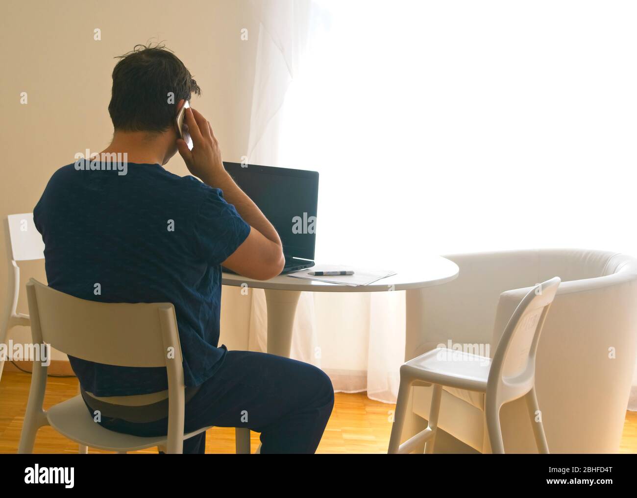 Jeune homme assis et travaillant sur un ordinateur portable à la maison parlant au mobile. Concept de père de travail. Concept de télétravail Banque D'Images