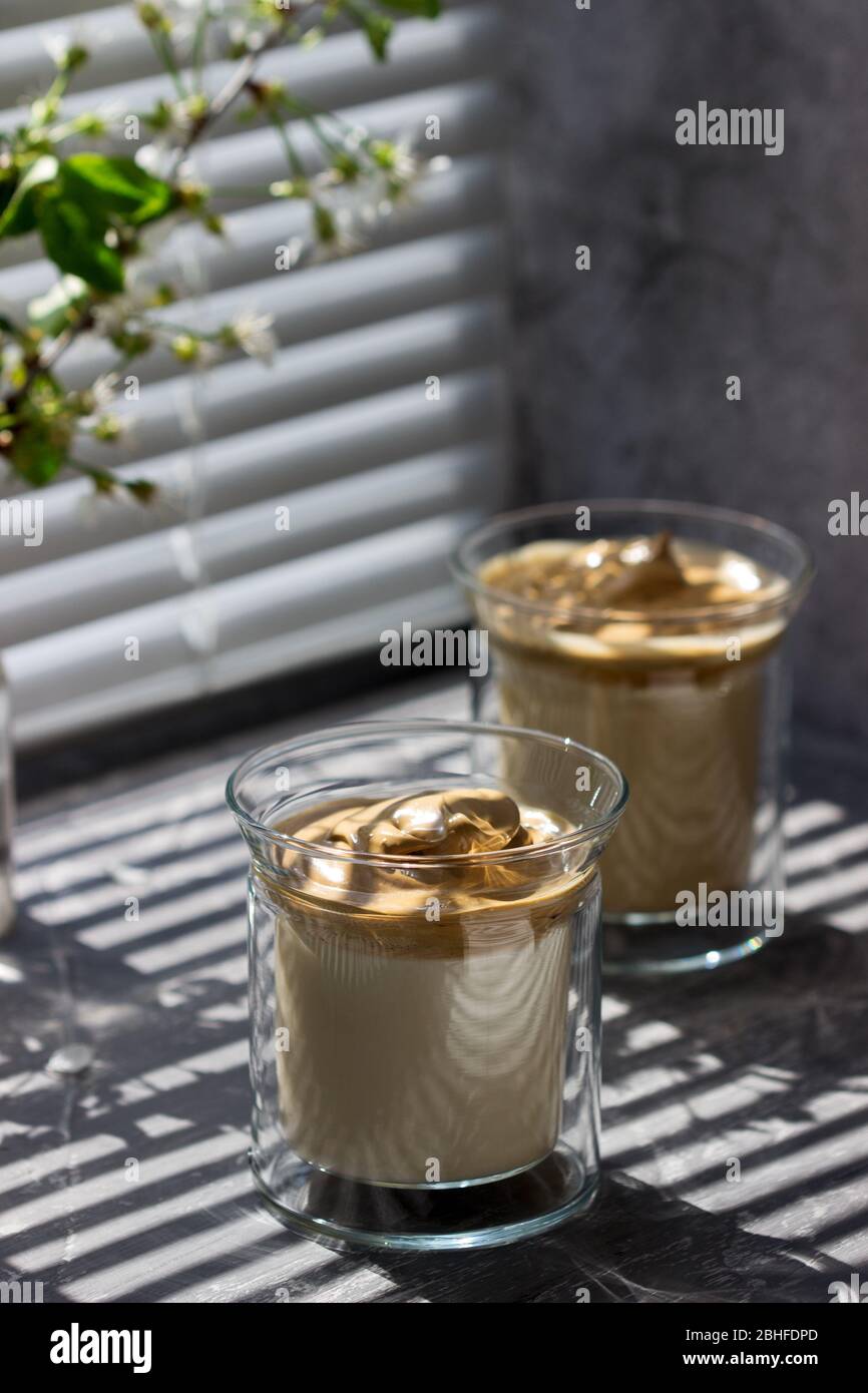 Dalgona café dans des verres transparents sur un seuil de fenêtre illuminé par la lumière du soleil. Banque D'Images