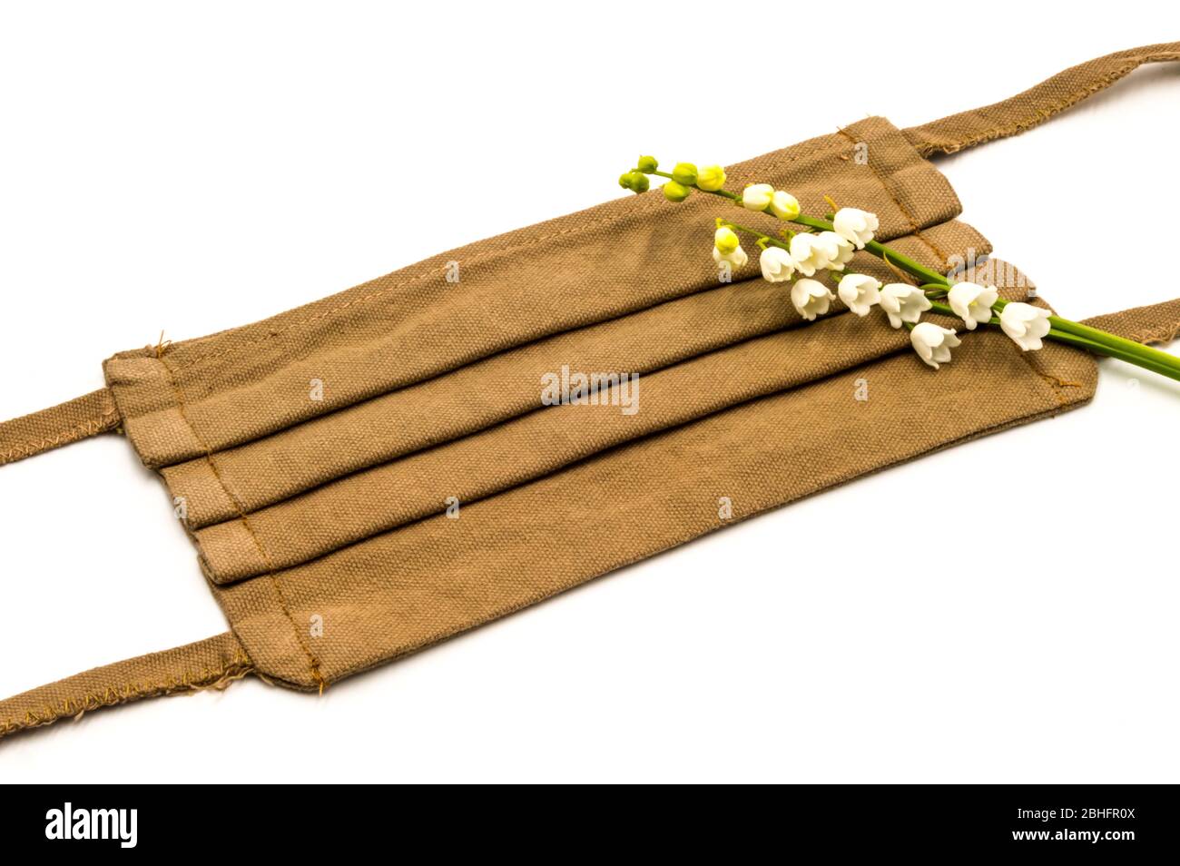 Toujours la vie d'un masque facial marron avec une branche de lys de la vallée sur un fond blanc anti covid 19, projet de couture de bricolage Banque D'Images Toujours la vie d'un masque facial marron avec une branche de lys de la vallée sur un fond blanc anti covid 19, projet de couture de bricolage Banque D'Images