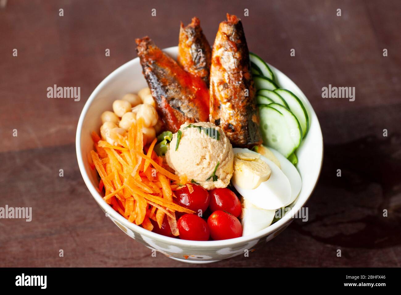 Salade colorée dans un bol blanc en chine avec des sardines, des carottes, du concombre, des œufs durs, des tomates cerises et des pois chiches Banque D'Images