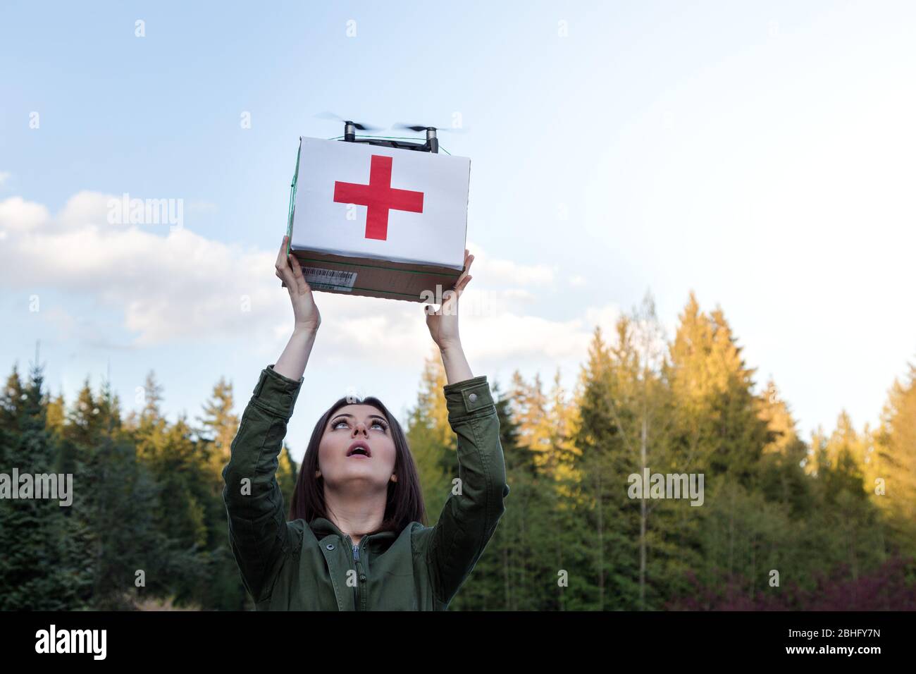 Jolie jeune femme brunette qui prend une boîte de fournitures médicales qui est livrée par un drone autonome. Banque D'Images