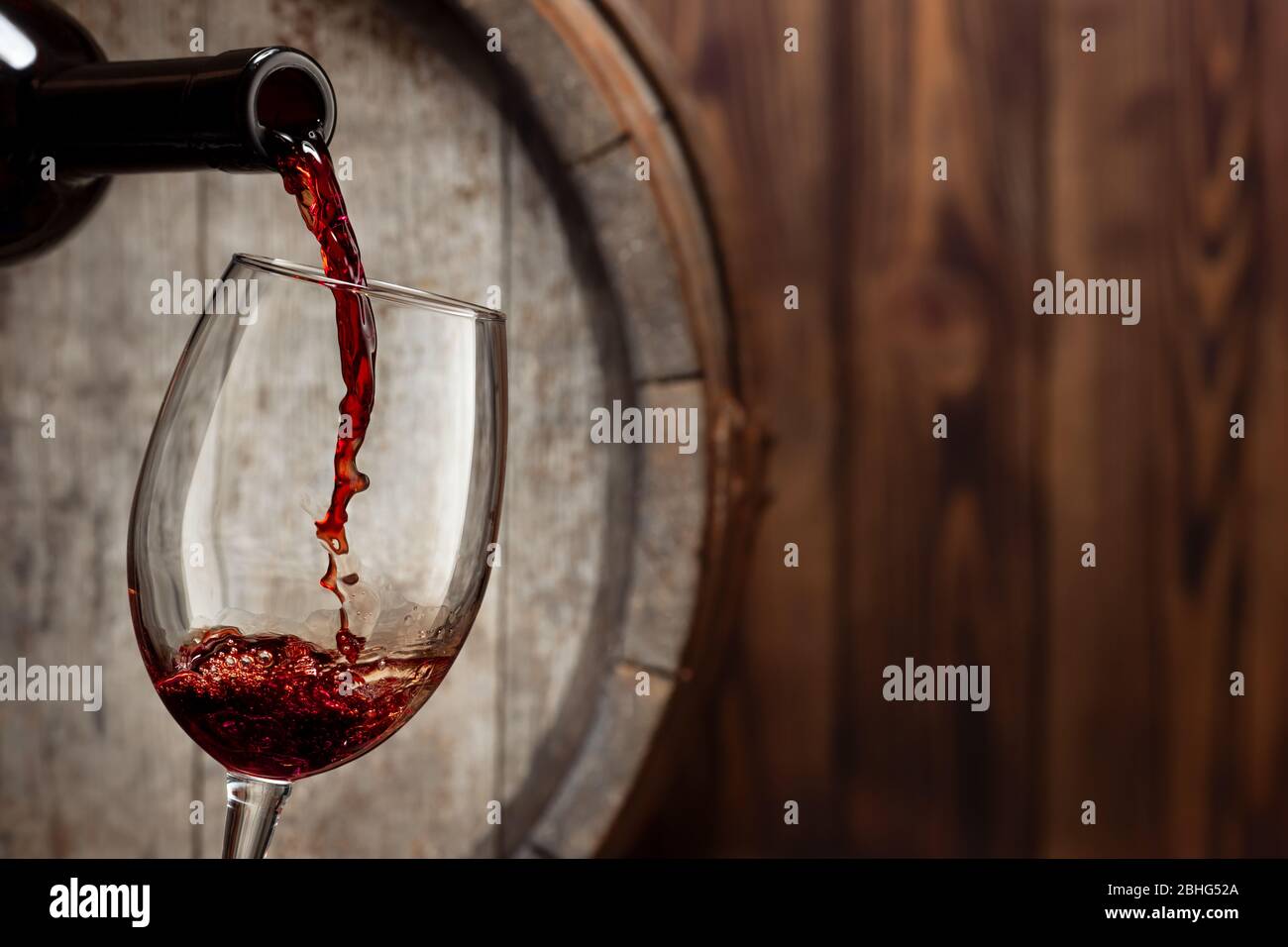 vin rouge qui coule de la bouteille dans le verre avec un vieux fût en bois  comme fond Photo Stock - Alamy