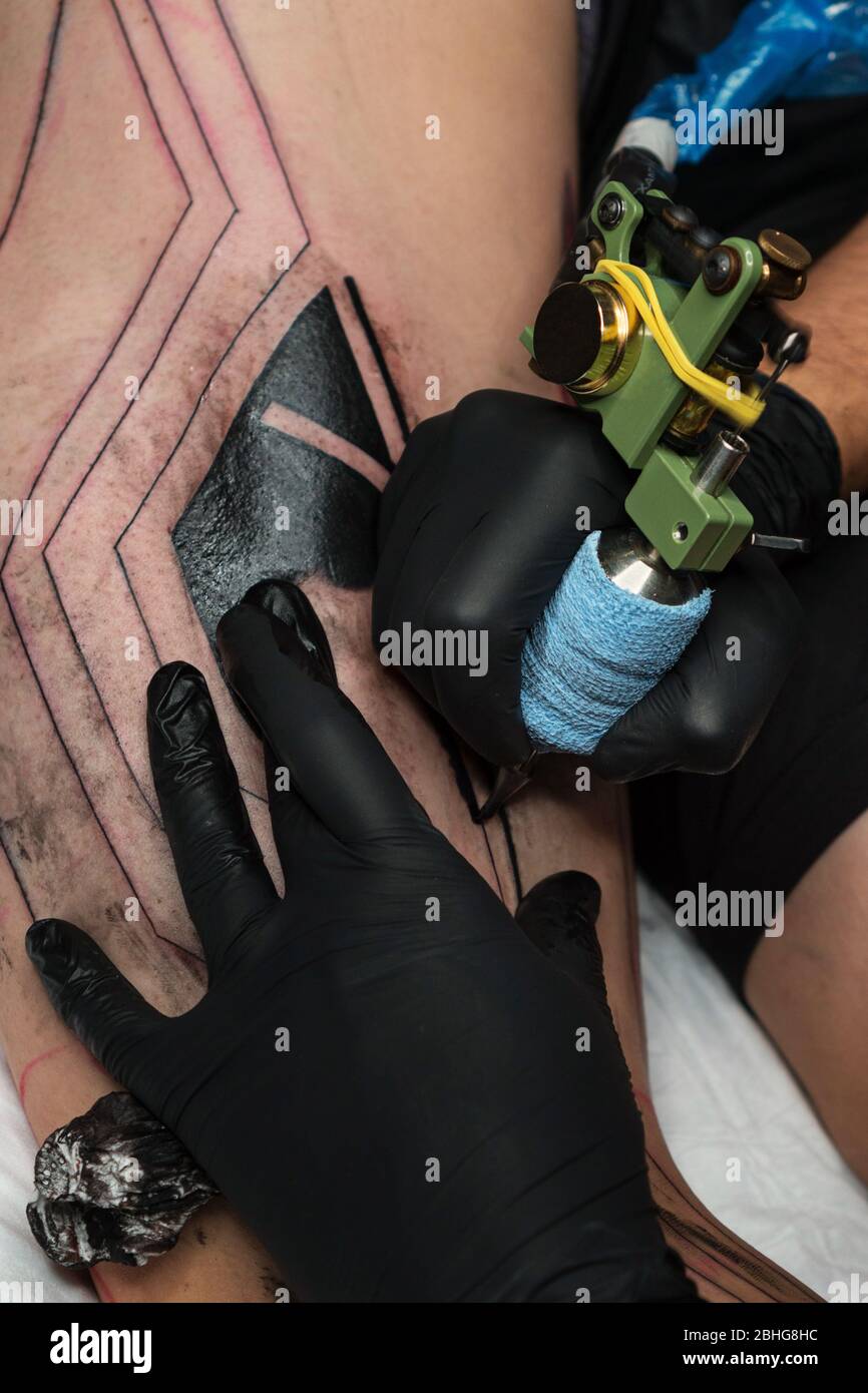 Un artiste professionnel de tatouage fait du tatouage sur la jambe de  l'homme. Processus. Introduit l'encre noire dans la peau à l'aide de  l'aiguille de la machine de tatouage. Gros plan sur