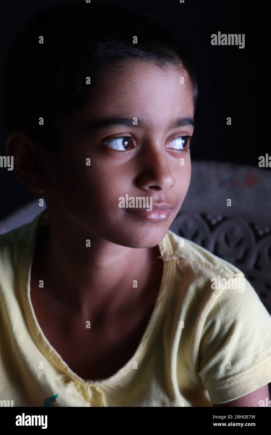 Portrait d'une petite fille indienne avec des cheveux courts. Bel œil d'un enfant sur fond noir. Un look dramatique d'une petite fille en Inde. Banque D'Images