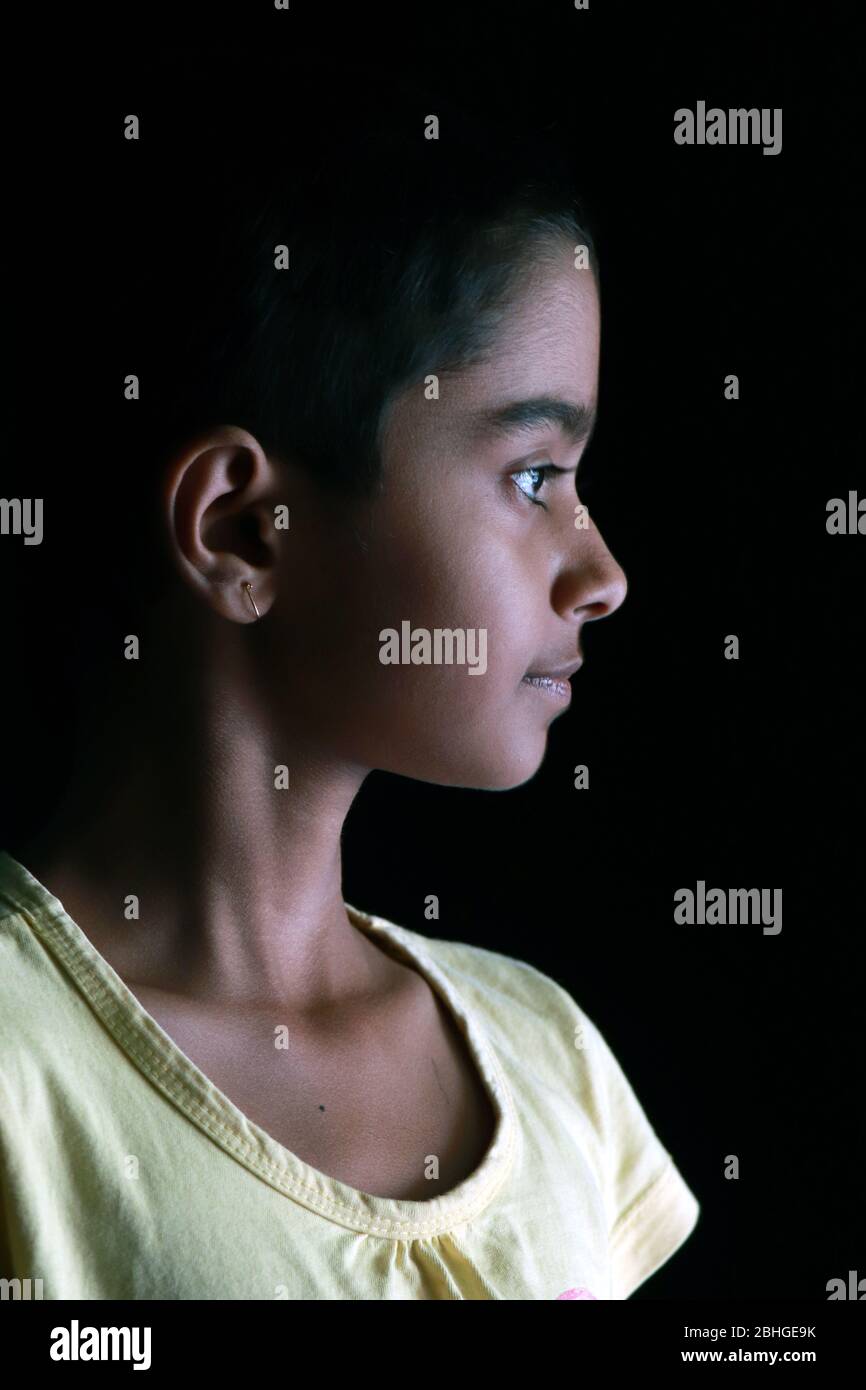 Portrait d'une petite fille indienne avec des cheveux courts. Bel œil d'un enfant sur fond noir. Un look dramatique d'une petite fille en Inde. Banque D'Images