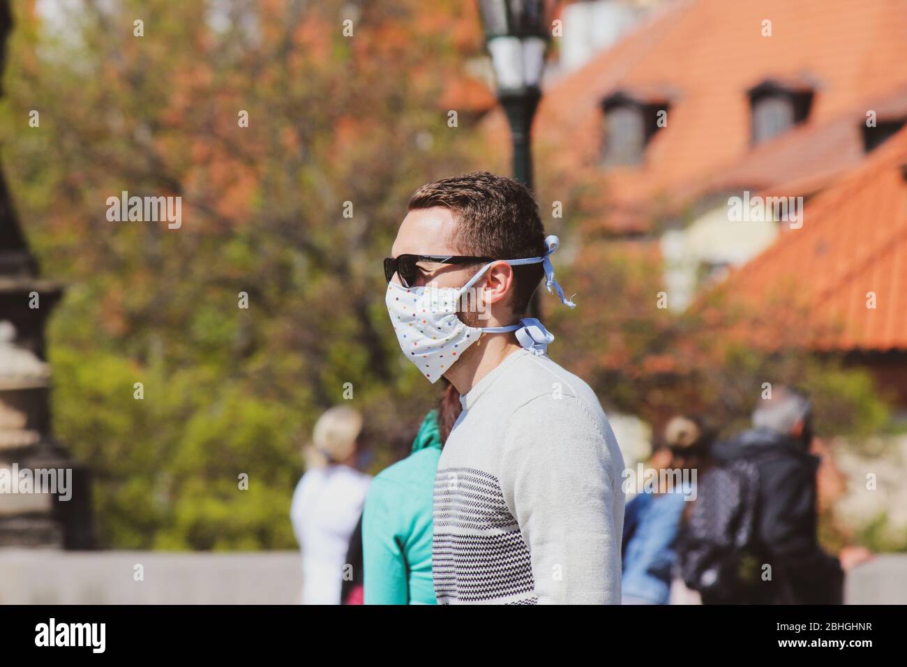 Jeune homme avec lunettes de soleil et masque en tissu cousu photographié sur le pont Charles à Prague, en République tchèque. Brouillé dans l'arrière-plan. Voyager, tourisme pendant coronavirus. COVID-19. Banque D'Images