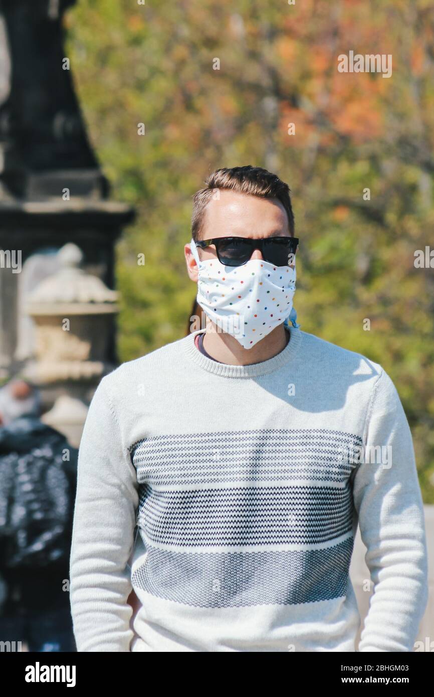 Jeune homme avec lunettes de soleil et masque en tissu cousu photographié sur le pont Charles à Prague, en République tchèque. Arrière-plan flou. Voyager, tourisme pendant coronavirus. COVID-19. Photo verticale. Banque D'Images