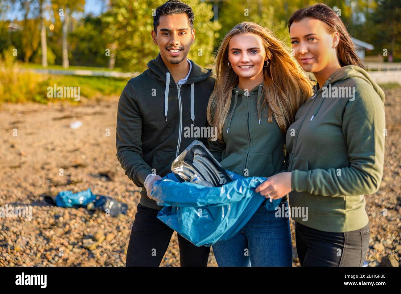 Des volontaires souriants tenant un sac à ordures à la plage Banque D'Images