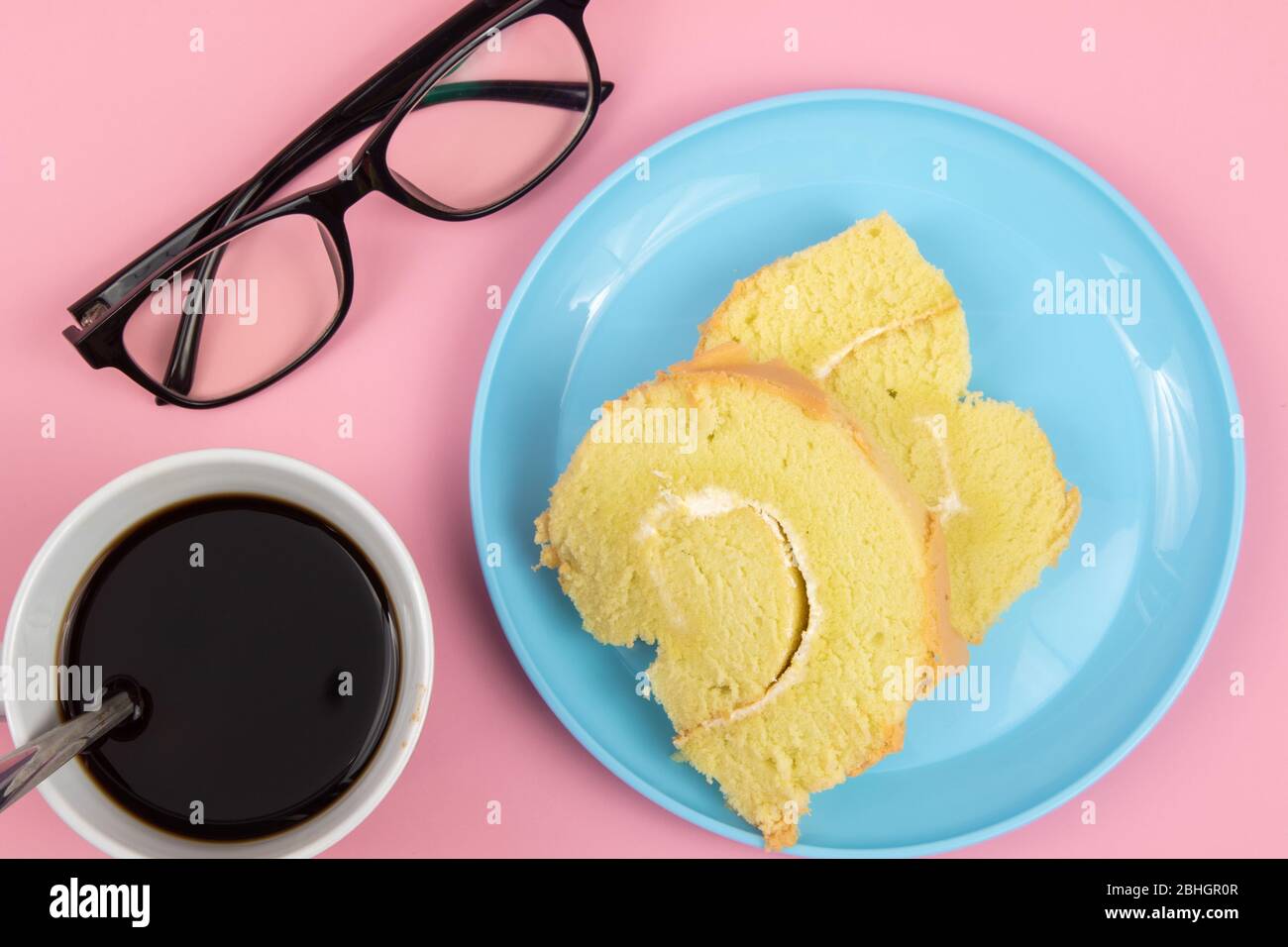 Lunettes lunettes, tranche de gâteau suisse à la rouette et tasse de café sur fond rose. Concept de pause-thé Banque D'Images