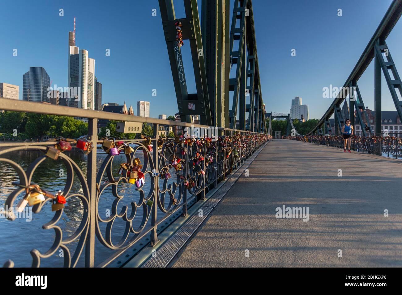 Un jogger en travers de Eiserner Steg pont de fer, à l'aube avec l'horizon de la ville de Francfort en toile affectueusement appelé love locks bridge Banque D'Images