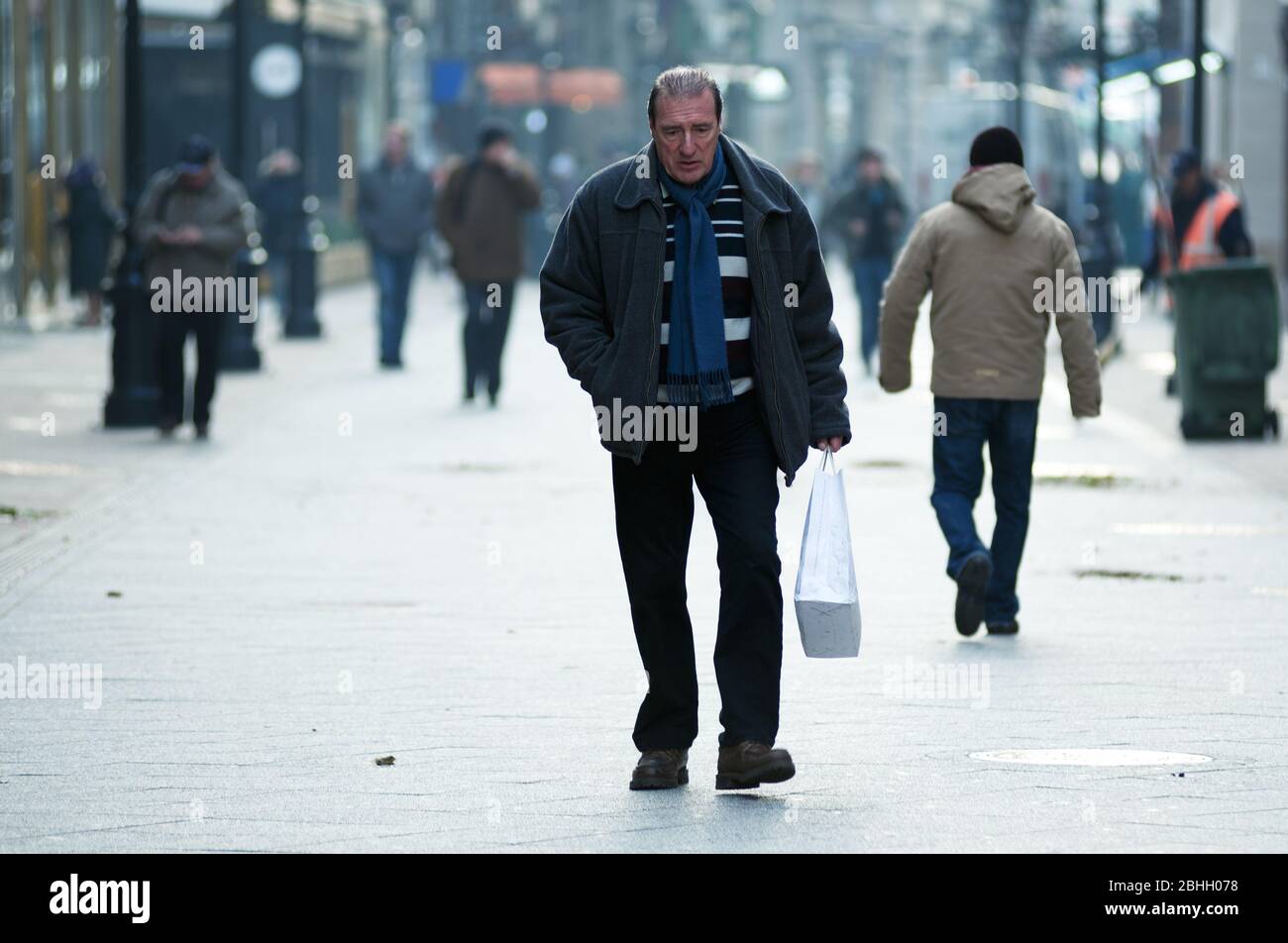 Triste homme marchant dans une rue de ville avec sac en plastique dans sa main Banque D'Images