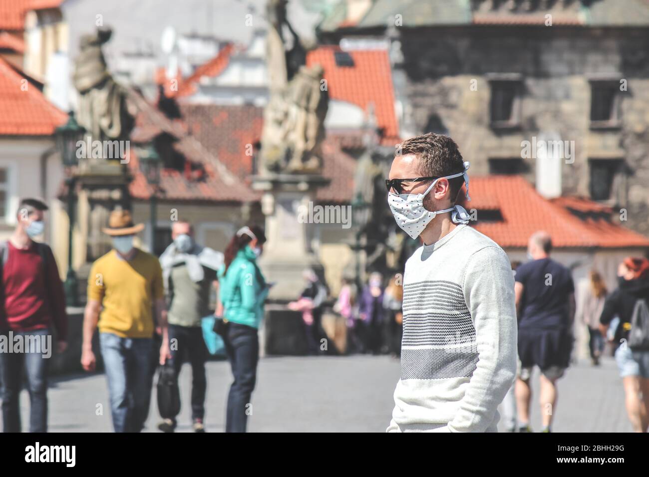 Jeune homme avec lunettes de soleil et masque en tissu cousu photographié sur le pont Charles à Prague, en République tchèque. Brouillé dans l'arrière-plan. Voyager, tourisme pendant coronavirus. COVID-19. Banque D'Images