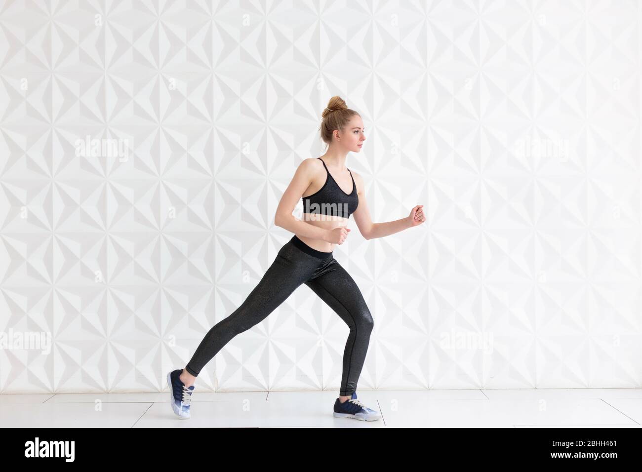 Jeune femme portant des vêtements de sport se posant près du mur blanc Banque D'Images