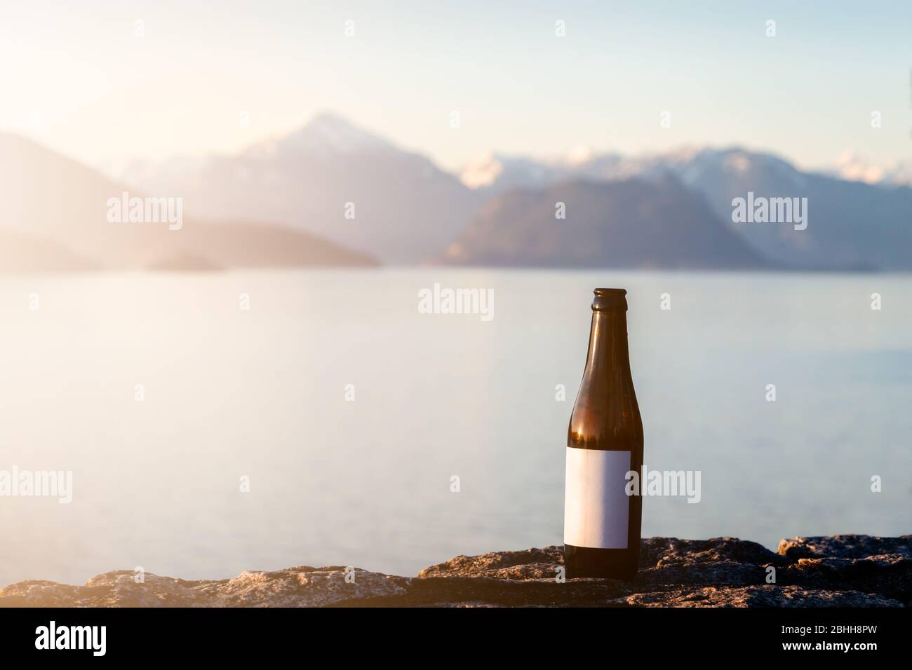 Une bière fraîche rafraîchissante avec étiquette vierge avec vue sur l'océan et un soleil. Banque D'Images