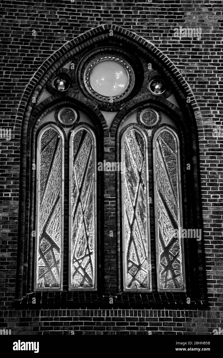 Ancienne fenêtre en arc sur un mur de briques en couleur monochrome. Un détail de proximité d'une église. Banque D'Images