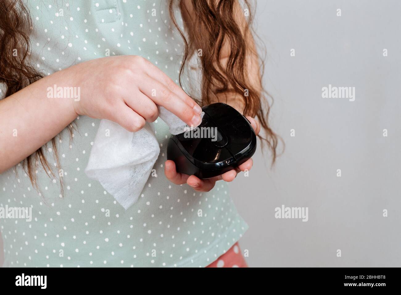 Une fille balaye une souris d'ordinateur avec un chiffon désinfectant. Arrêter la propagation du coronavirus COVID-19. Banque D'Images