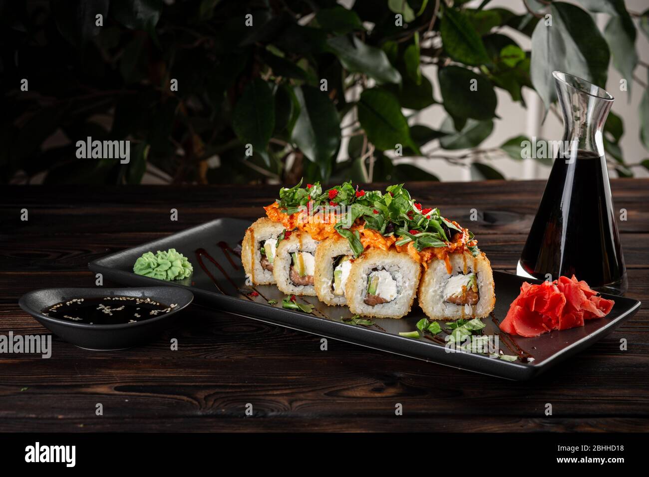 jeu de rouleaux de sushi sur une plaque noire rectangulaire avec sauce soja et baguettes sur fond en bois noir Banque D'Images