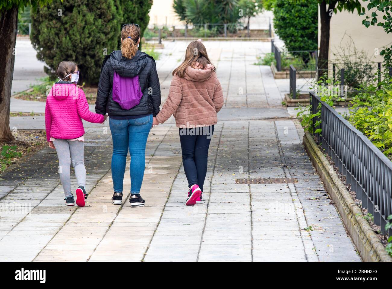 Une mère descend la rue avec ses deux filles portant des masques Banque D'Images