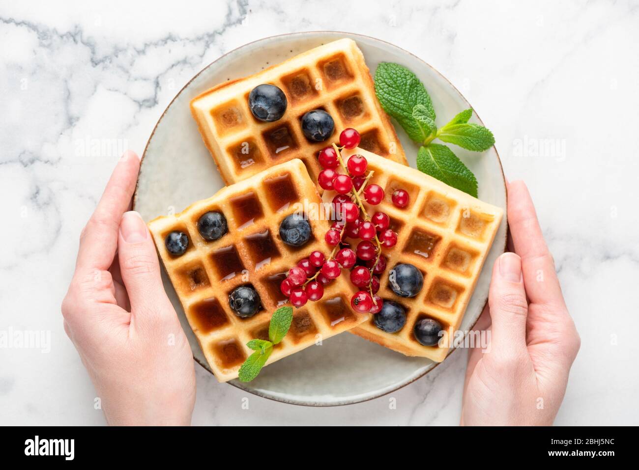 Assiette de gaufres belges avec baies et sirop dans les mains des femmes, vue de dessus. Délicieux petit déjeuner sucré Banque D'Images