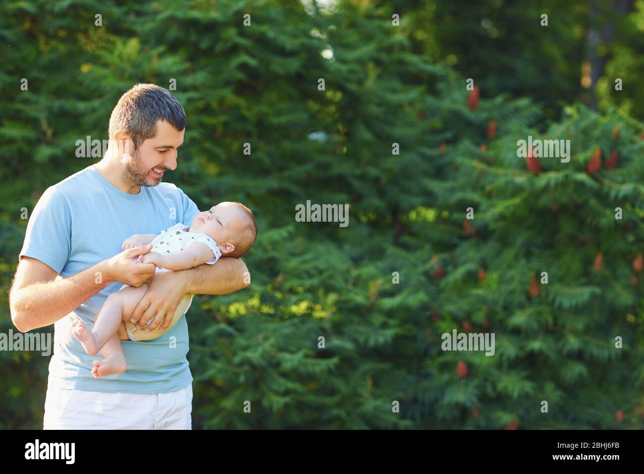 Fête des pères. Le père bienveillant tient le bébé dans ses bras dans le parc sur fond de feuilles vertes. Banque D'Images