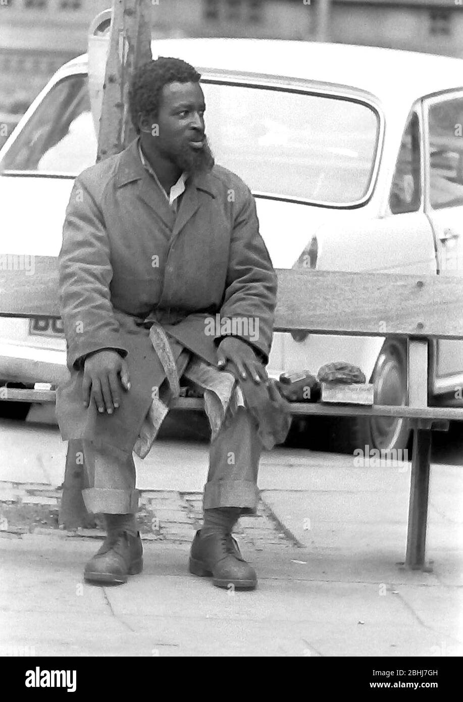 La vie quotidienne dans les rues de Manchester, Angleterre, Royaume-Uni en 1974. Un homme afro Caribbean est assis sur un banc à Albert Square, dans le centre de Manchester. Banque D'Images