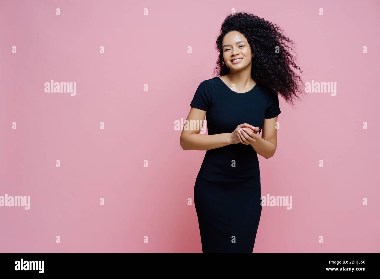 Photo de heureuse gaie sombre peau maudit robes pour un événement décontracté, sourires positivement, aime parler agréable avec l'homme, garde les mains ensemble, sta Banque D'Images