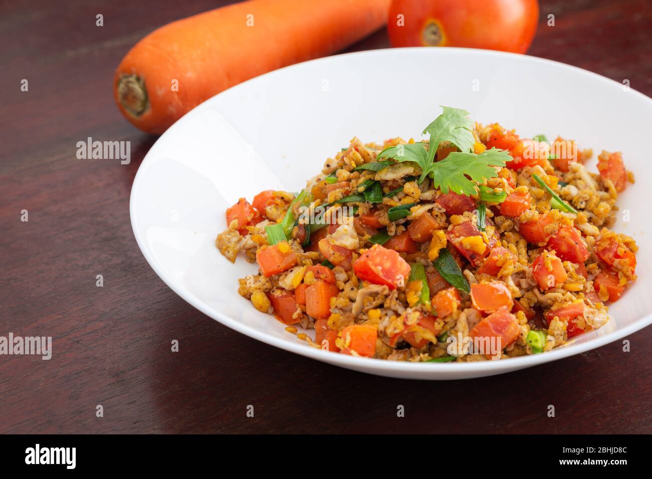 Œufs brouillés faits maison avec carottes et tomates en plaque blanche sur table en bois. Banque D'Images Œufs brouillés faits maison avec carottes et tomates en plaque blanche sur table en bois. Banque D'Images
