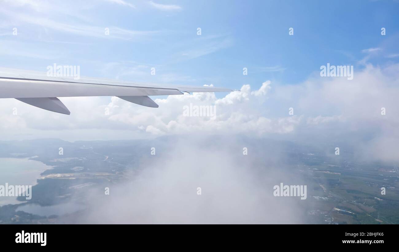 aile d'avion volant à travers des nuages au-dessus de la terre de recul avec des villes rivières montagnes contre le ciel avec des nuages blancs Banque D'Images