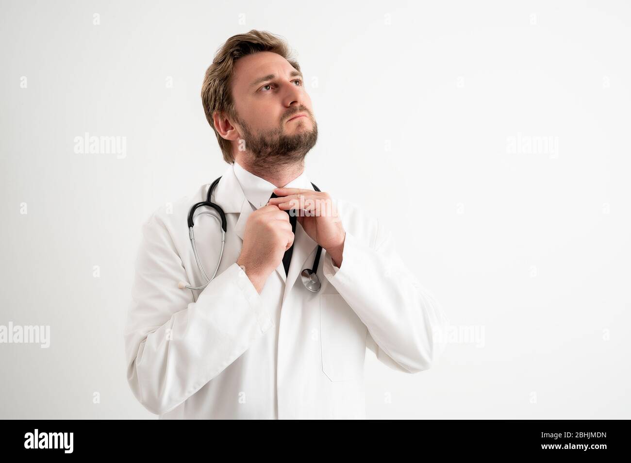 Portrait du médecin mâle avec stéthoscope en uniforme médical organise sa cravate posant sur un fond blanc isolé. Banque D'Images