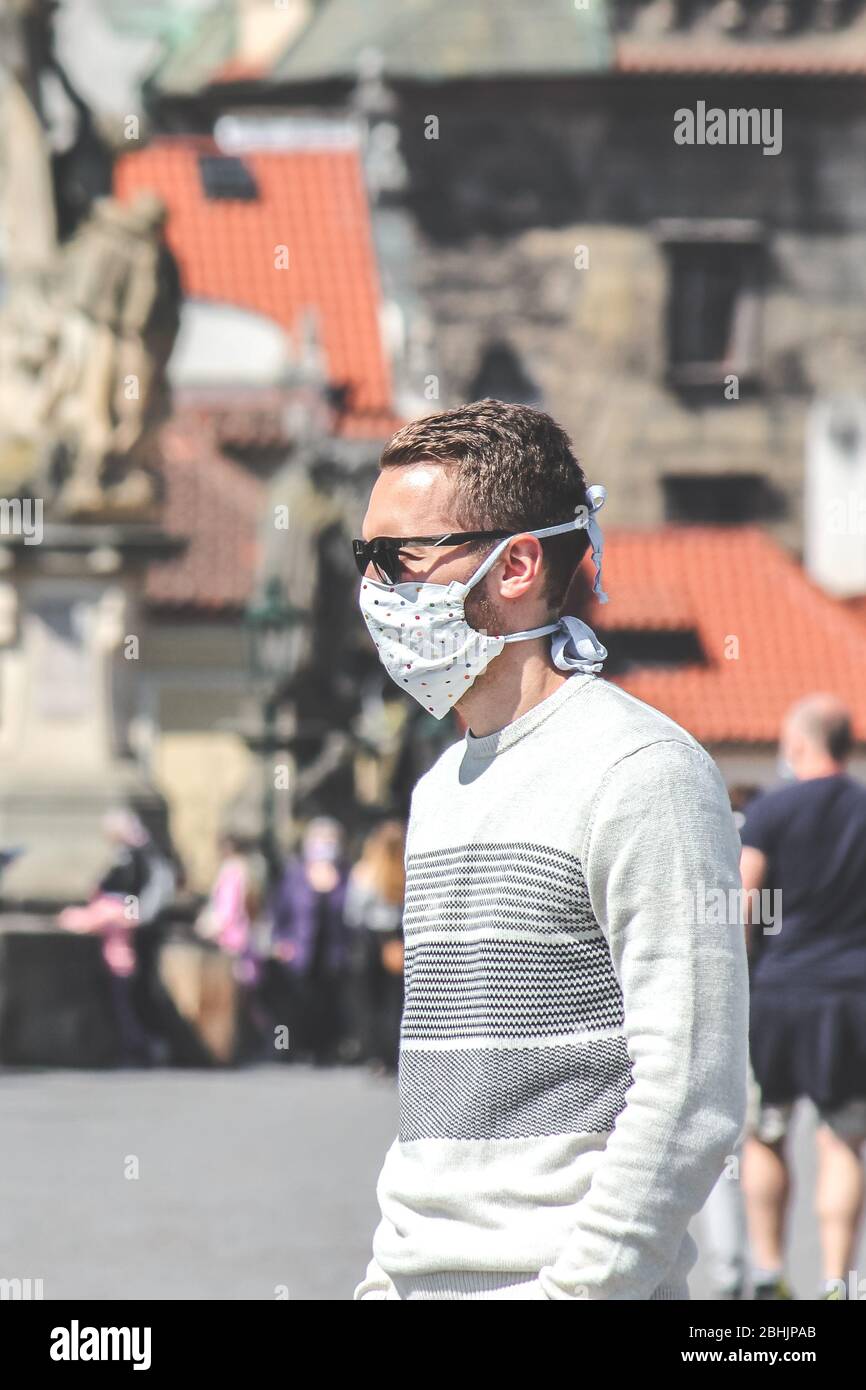 Jeune homme avec lunettes de soleil et masque en tissu cousu photographié sur le pont Charles à Prague, en République tchèque. Brouillé dans l'arrière-plan. Voyager, tourisme pendant coronavirus. COVID-19. Banque D'Images
