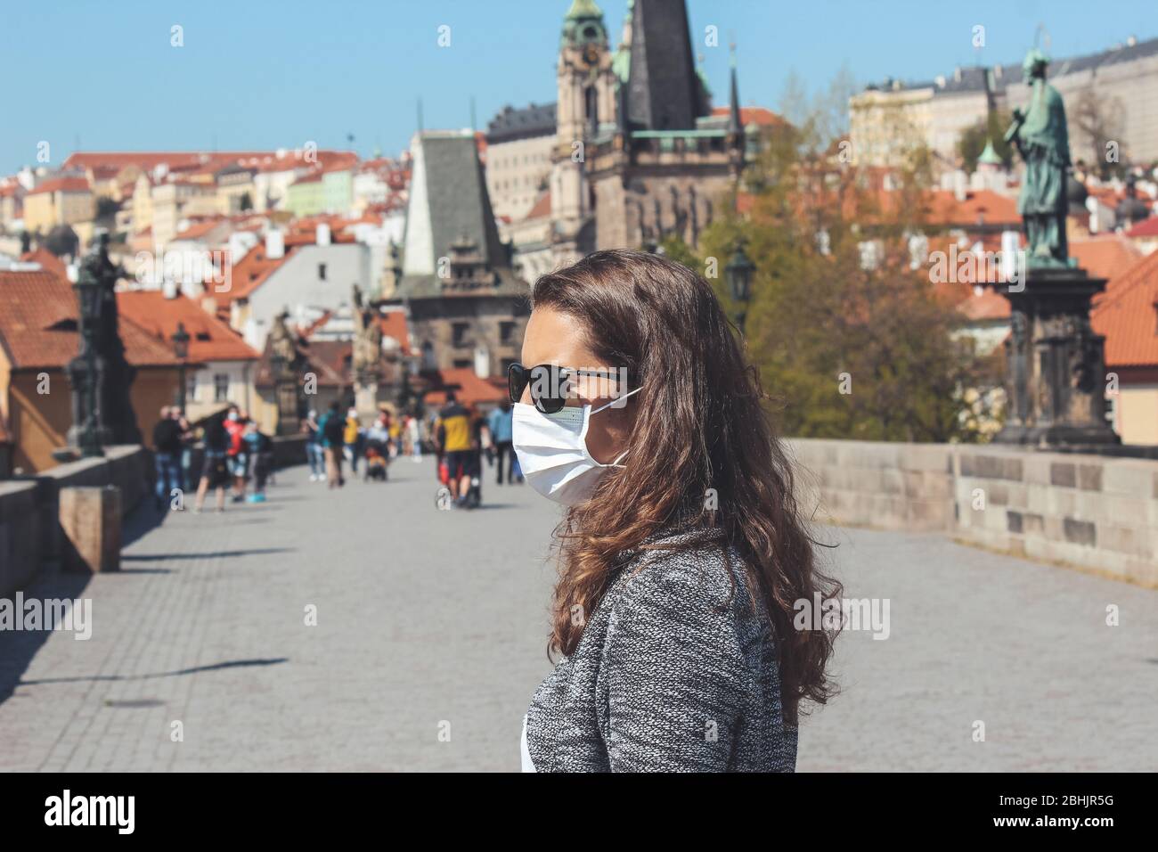 Jeune femme avec lunettes de soleil et masque médical photographié sur le pont Charles à Prague, République tchèque. Vieille ville floue à l'arrière-plan. Voyager, tourisme pendant coronavirus. COVID-19. Banque D'Images