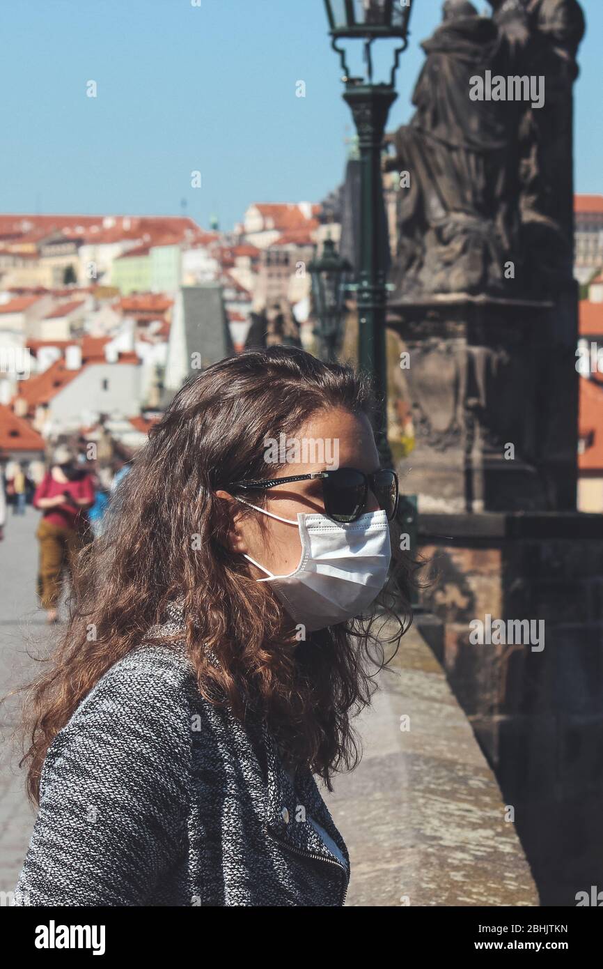 Jeune femme avec lunettes de soleil et masque médical photographié sur le pont Charles à Prague, République tchèque. Les gens sont floutés et la vieille ville en arrière-plan. Tourisme pendant le coronavirus. COVID-19. Banque D'Images